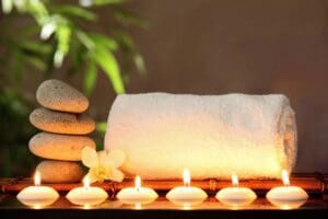 four stacked stones beside a rolled towel and behind lit candles