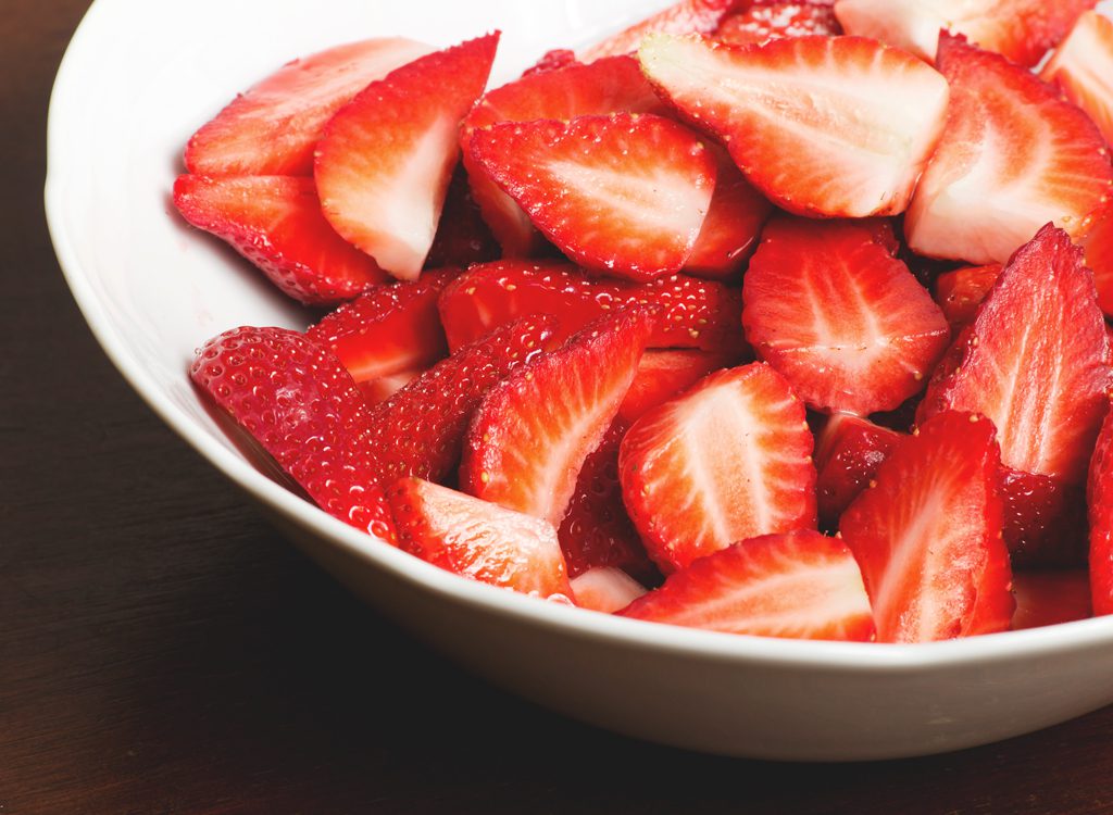 A bowl of sliced strawberries on top of a table.